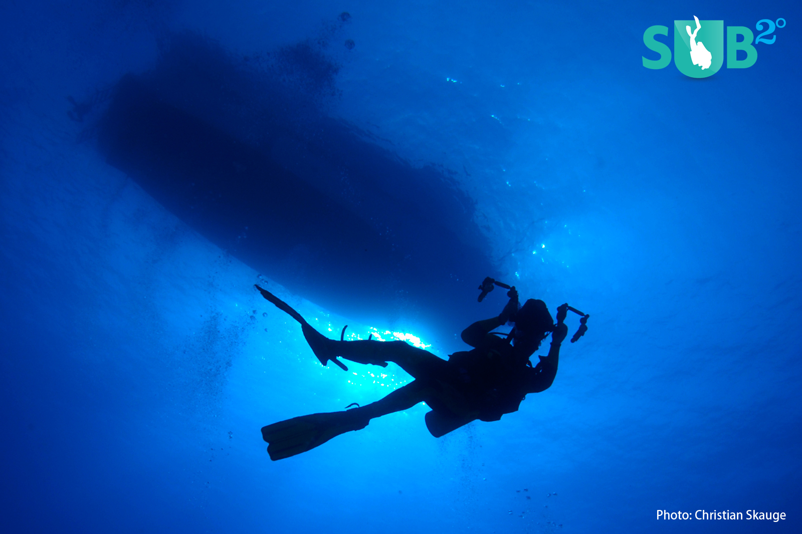 A diver in perfect silhouette against the blue water, with the dive boat at the surface.